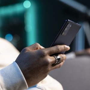 Close up shot on smartphone held by person sending messages to internet mates, enjoying himself at home. Focus on phone used by man in blurry background to catch up with friends